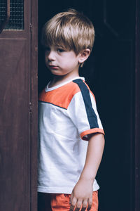 Boy looking away while standing against door