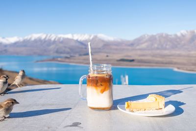 Birds perching by dessert on table with lake in background