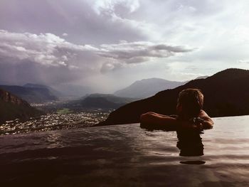Young woman sitting on mountain against sky