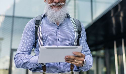 Senior hipster holding digital tablet against building