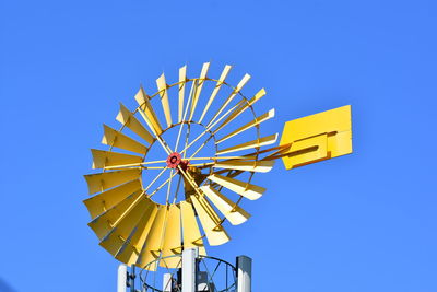 Low angle view of water wheel against clear blue sky