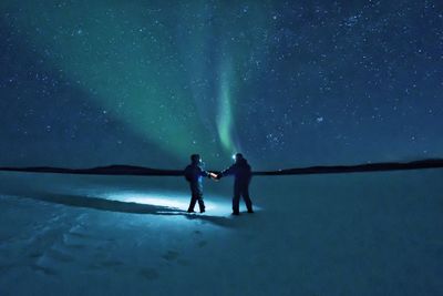 People on snowy land against sky at night