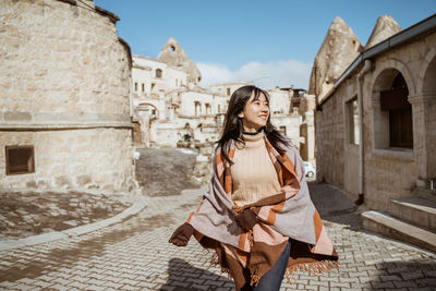 Portrait of young woman standing against building