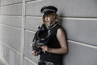Young woman holding equipment against wall during cosplay