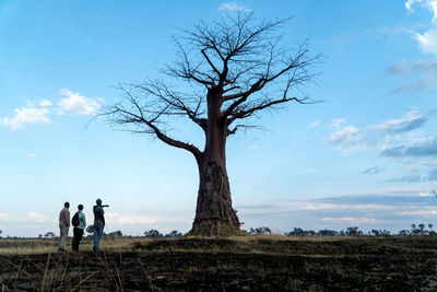 People standing by bare tree on field against sky