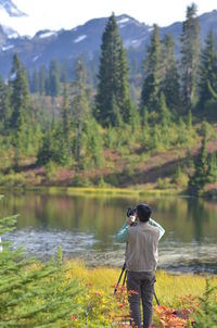 Rear view of man photographing lake against trees