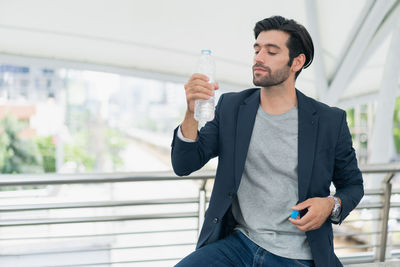 Young man drinking water while standing in city