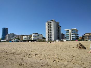 Beach by buildings against clear blue sky