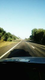 Road amidst trees against clear sky seen through car windshield