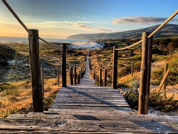 Wooden boardwalk leading towards mountains against sky