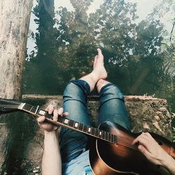 Low section of woman playing guitar over lake