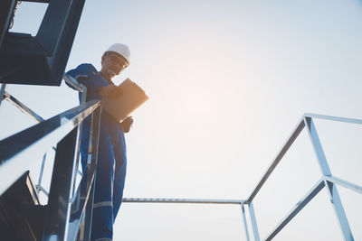 Low angle view of man working against clear sky