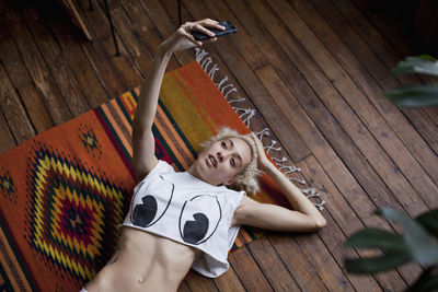 Young woman taking selfie while lying on wooden floor at home