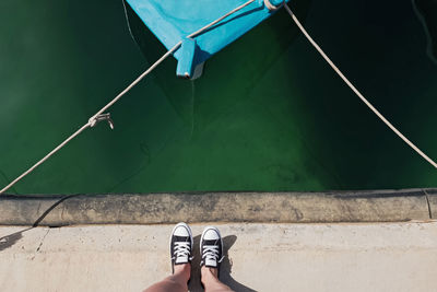 Feminine feet in black and white sneakers standing near the water and boat in marine. 