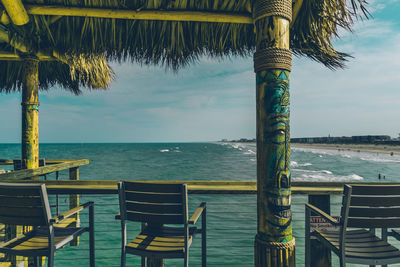 Close-up of chairs on table by sea against sky