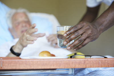 Cropped image of male nurse giving drinking glass to senior man in hospital ward