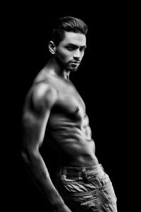 Portrait of shirtless man standing against black background