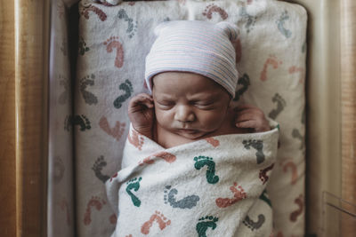 Overhead view of newborn boy with hat in hospital bassinet