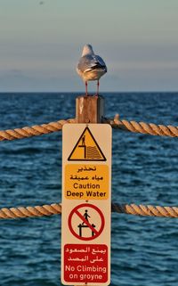 Close-up of warning sign on sea against sky