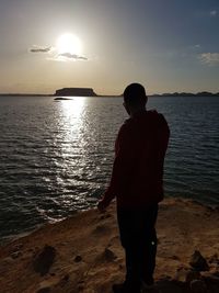 Rear view of silhouette man looking at sea against sky during sunset