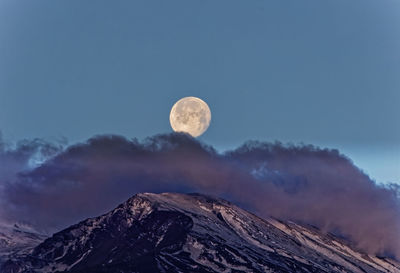 Low angle view of the snowy peak of etna volcano with moon setting