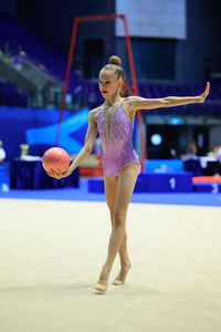 A rhythmic gymnast performs with a ball, displaying artistry and athleticism at a competition