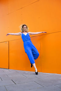 Full length of woman dancing against orange wall