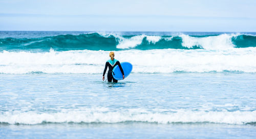 Woman with surfboard wading in sea against sky