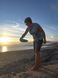 Full length of woman holding plastic disc at beach during sunset