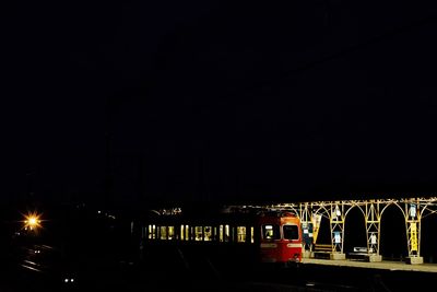 Train by illuminated railroad station against clear sky at night