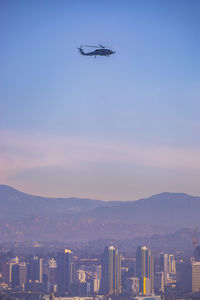 Helicopter flying over cityscape and mountains against sky