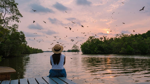 Rear view of woman standing by lake against sky during sunset