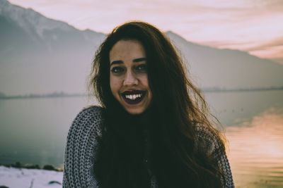 Portrait of smiling young woman standing against lake