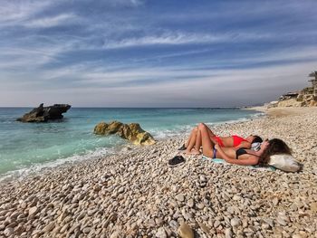 Man lying on rock at beach against sky