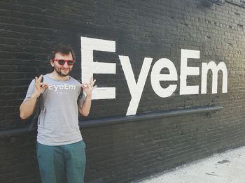 Portrait of young man standing by text on wall