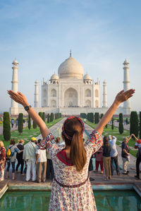 Girl with arms raised standing against taj mahal