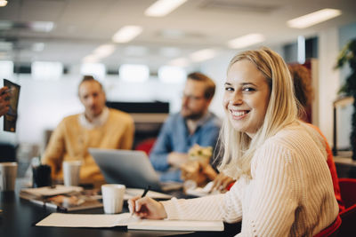 Portrait of smiling young businesswoman sitting with colleagues at conference table in office