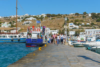 People at harbor by city against clear sky