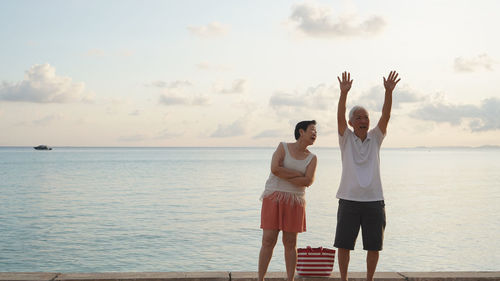 Friends standing at sea shore against sky