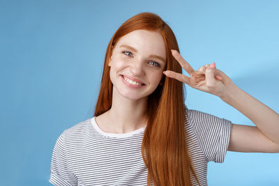 Woman making victory sign against blue background
