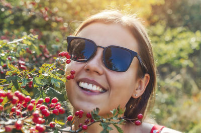 Portrait of young woman in sunglasses on nature near bush with red berries. smile, natural