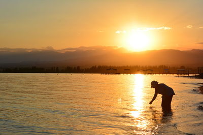 Silhouette man standing in sea against sky during sunset