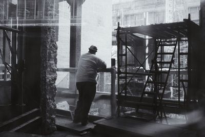 Full length rear view of construction worker standing at incomplete building