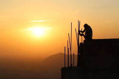 Silhouette man standing on mountain against orange sky