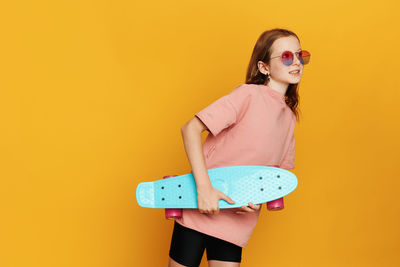 Portrait of young woman wearing sunglasses standing against yellow background