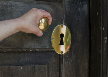 Cropped hand holding golden doorknob on wooden door