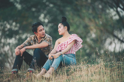 Young woman looking away while sitting on field