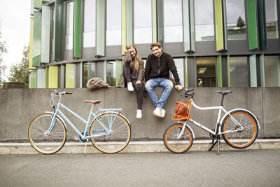 Happy couple with bicycles sitting on a wall