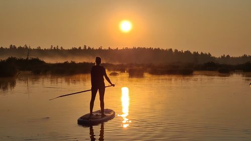 Rear view of woman standing in lake against sky during sunset. sunset on sup