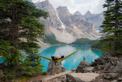 High angle rear view of man resting on hammock in front of lake in mountainous landscape